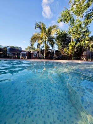 A clear swimming pool with a tiled bottom, surrounded by palm trees and buildings. - Cabañas Rosedal Cataratas (Puerto Iguazú)