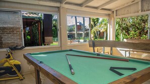 Ein Billardtisch mit grüner Spielvliesbahn, ein gelbes Fitnessrad und Blick auf eine Terrasse mit Sitzgelegenheiten.