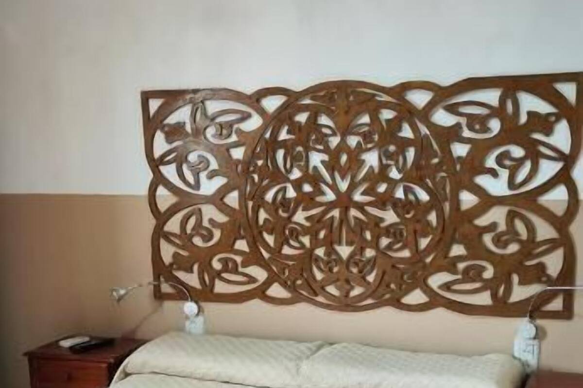 Una cama con colcha acolchada, cabecera de madera con intrincados grabados y mesita de noche con lámpara.