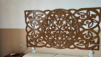 Uma cama com colcha acolchoada, cabeceira de madeira com esculturas detalhadas e uma mesa de cabeceira com abajur.