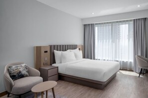 Una habitación de hotel moderna con una cama grande, una mesita de noche, una silla y una pequeña mesa.