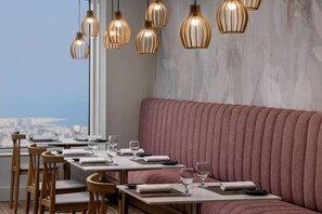 Un ristorante con vista sulla città, tavoli in legno e una panca imbottita rosa.