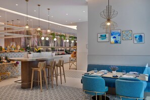 Un ristorante moderno con zona bar, sedute blu e illuminazione a sospensione.