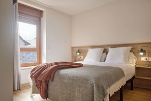 Ein Schlafzimmer mit einem Bett, zwei Nachttischlampen, einem Fenster und einem hölzernen Kopfteil.