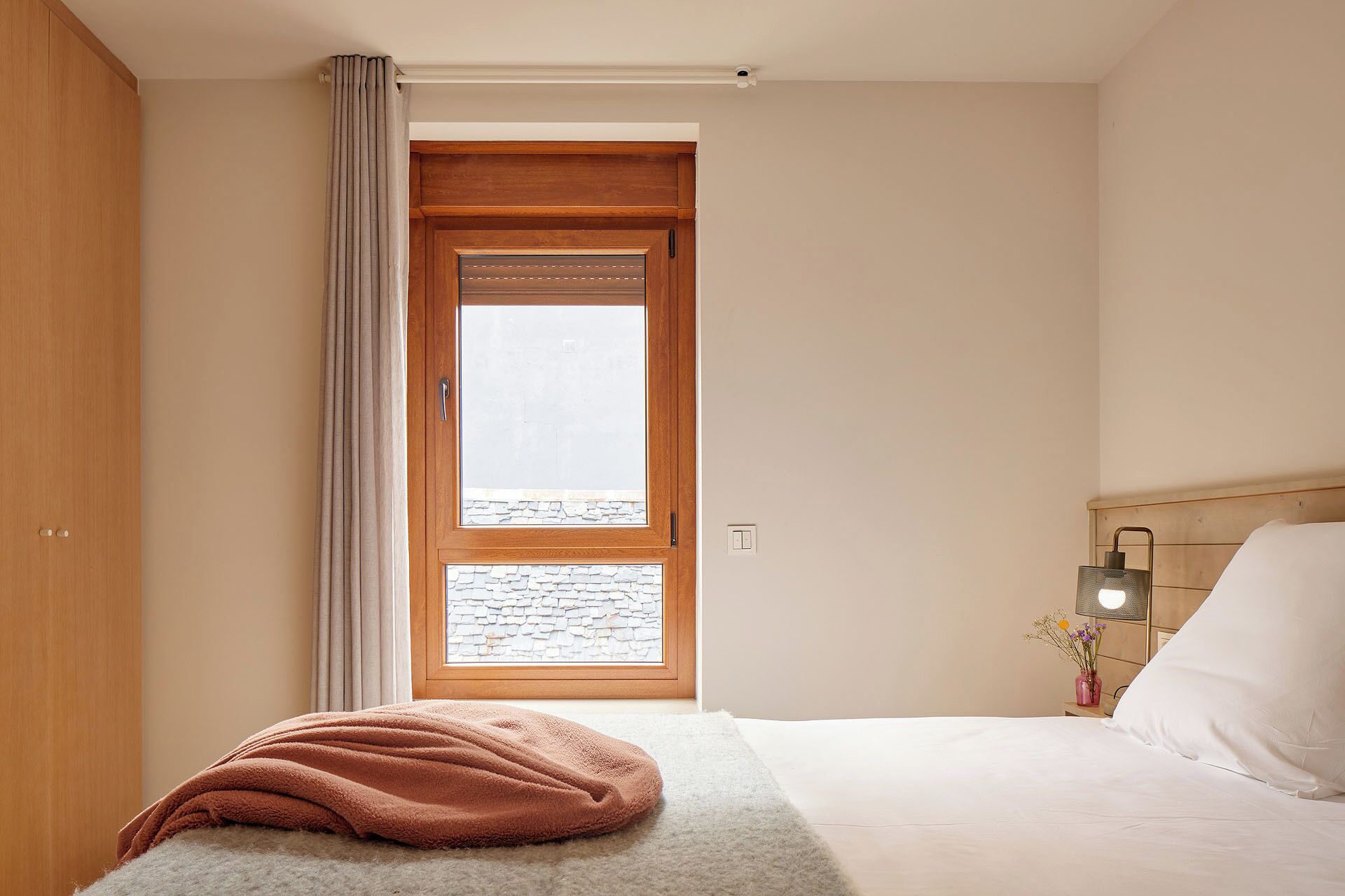 Une chambre à coucher avec un lit, une table de chevet, une lampe, une fenêtre donnant sur un beau paysage et une porte.