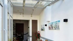 A sunlit corridor with wicker chairs, a glass ceiling, and a dining area with a table and chairs. - Hotel Runge 24-7 check in & free parking (Kiel)
