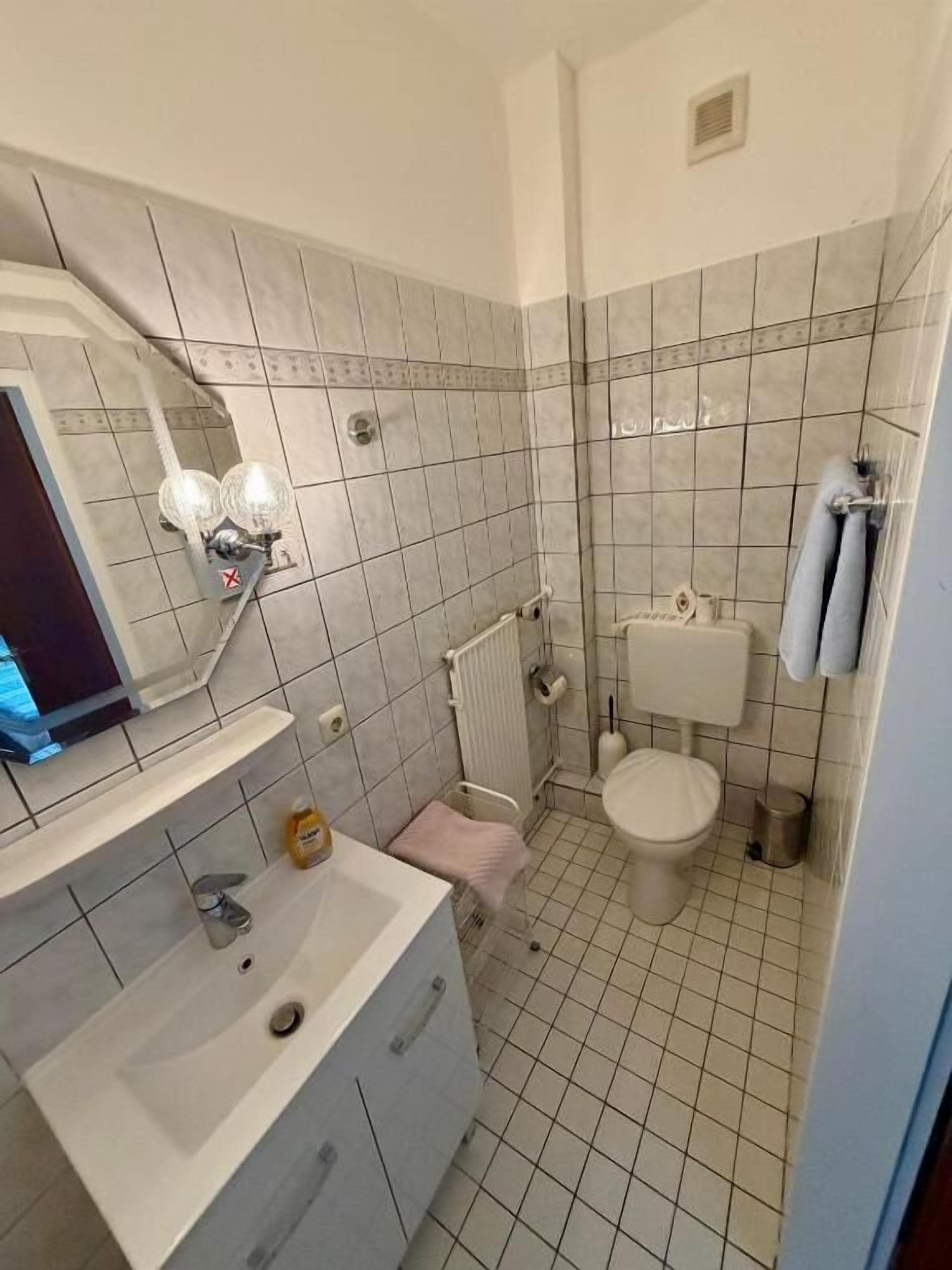 Kylpyhuone, jossa on valkoinen pesuallas, peili ja wc-istuin.