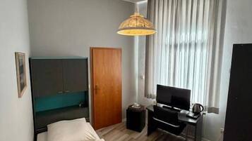 A compact hotel room with a bed, a desk with a computer, a television, and a window with curtains.