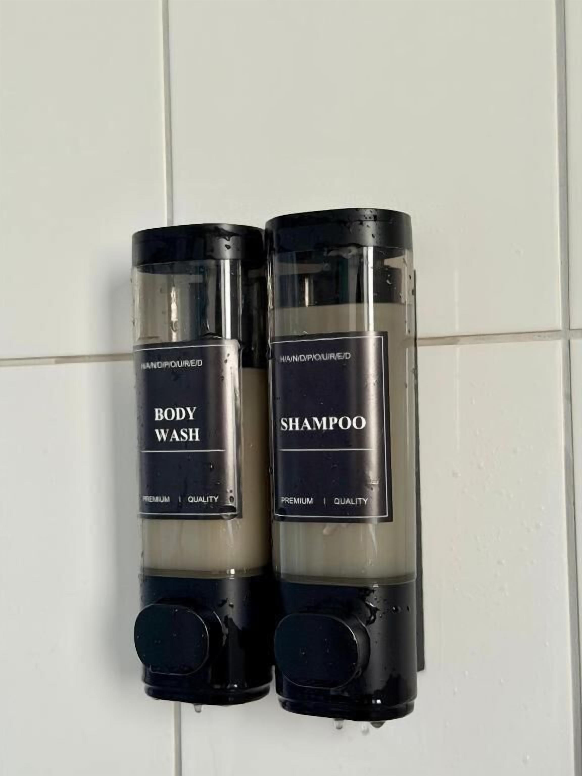 Two hand-poured dispensers for body wash and shampoo mounted on a tiled wall.