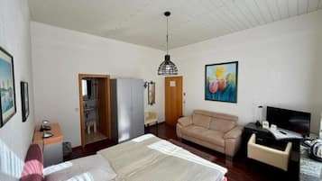 Une chambre à coucher comprenant un lit, un bureau, un canapé, une télévision et une porte donnant sur une salle de bain.