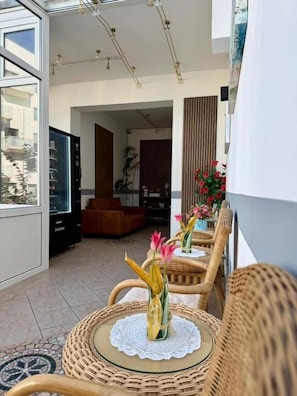 A balcony with wicker chairs, a glass table, and a view of the building's interior. - Hotel Runge 24-7 check in & free parking (Kiel)