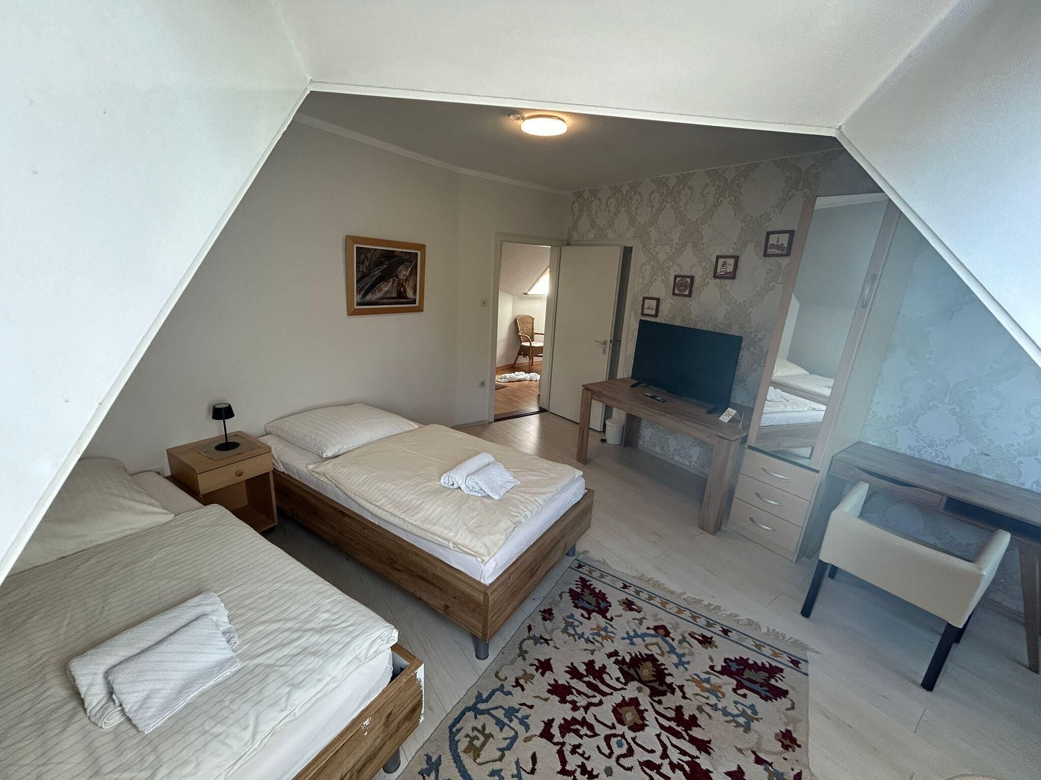 Une pièce triangulaire comprenant deux lits, un bureau, une télévision et un tapis à motifs.