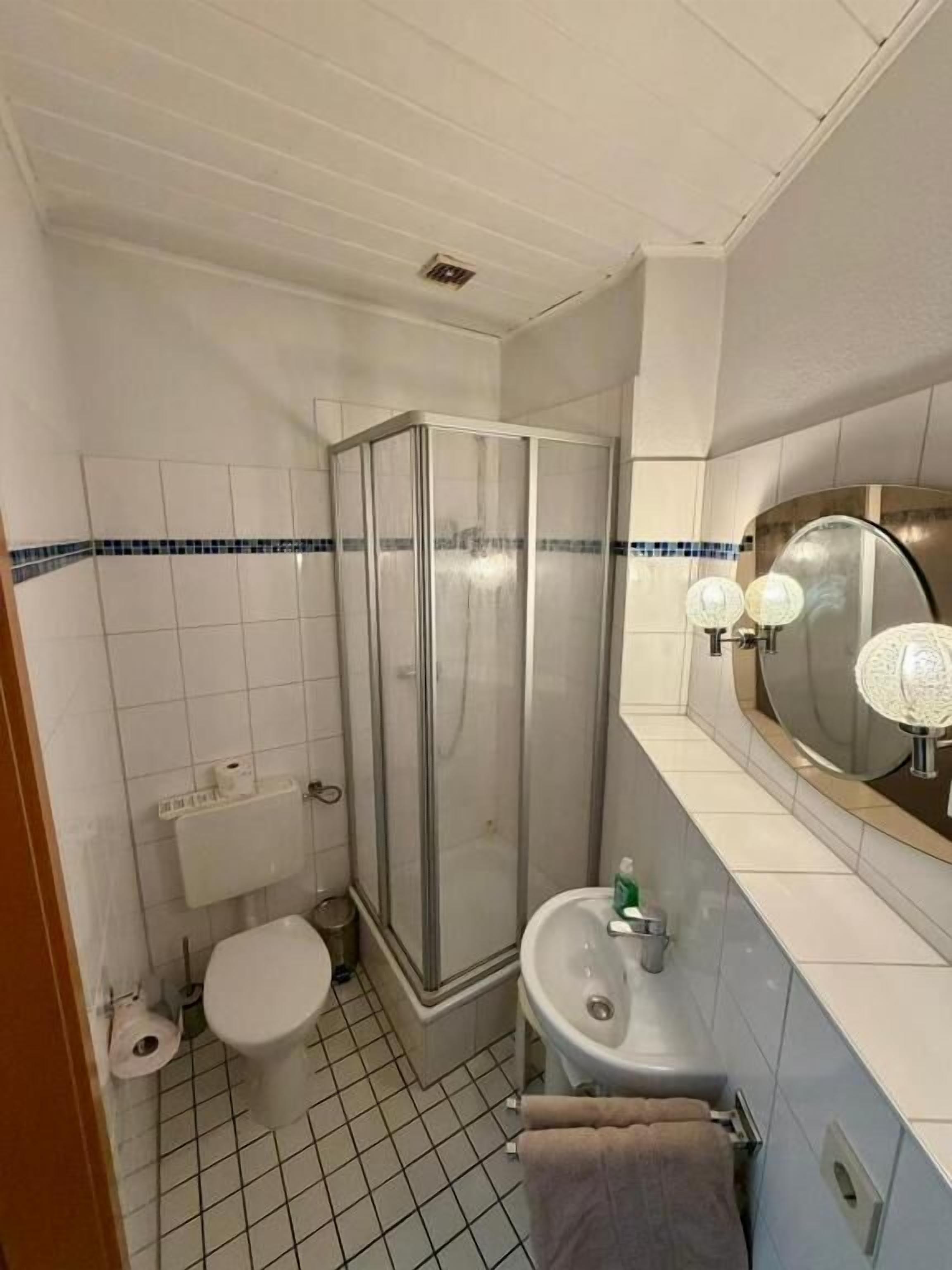Un baño con inodoro, ducha, lavamanos y espejo con iluminación.