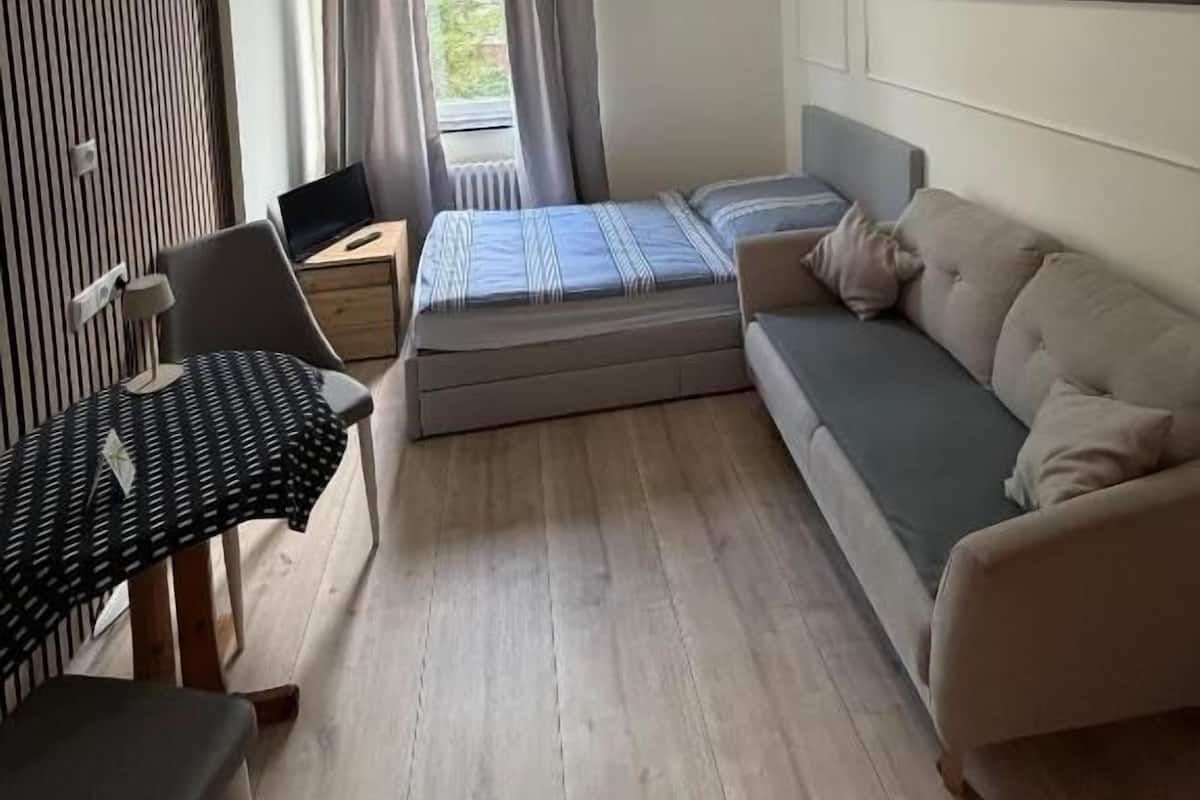 Una habitación con cama, sofá, escritorio y ventana con cortinas.