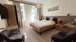 A modern bedroom with a bed, two chairs, a desk, a TV, and a window with curtains. - Hotel Runge 24-7 check in & free parking (Kiel)