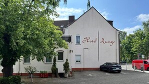 A building with a sign reading 'Hotel Rungce' and a parking area with a car and a red van. - Hotel Runge 24-7 check in & free parking (Kiel)