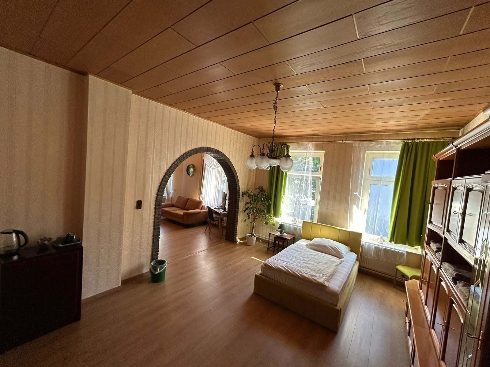 Een ruime kamer met een houten plafond, een bed, een bureau, een stoel en een groene plant.