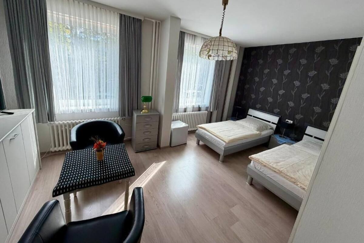 Habitación de hotel con escritorio, dos camas, una silla, radiador y ventana con cortinas.