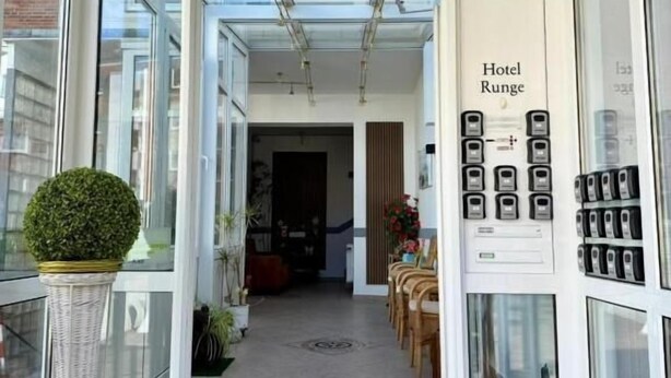 A hotel entrance with a glass door, a reception desk, a sign reading 'Hotel Runge,' and a row of phones on the wall. - Hotel Runge 24-7 check in & free parking (Kiel)