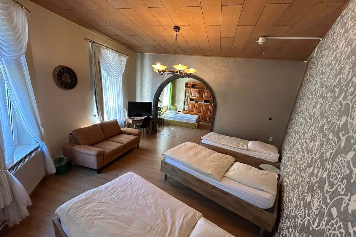 Una habitación con sofá, dos camas individuales, televisor, escritorio y espejo.