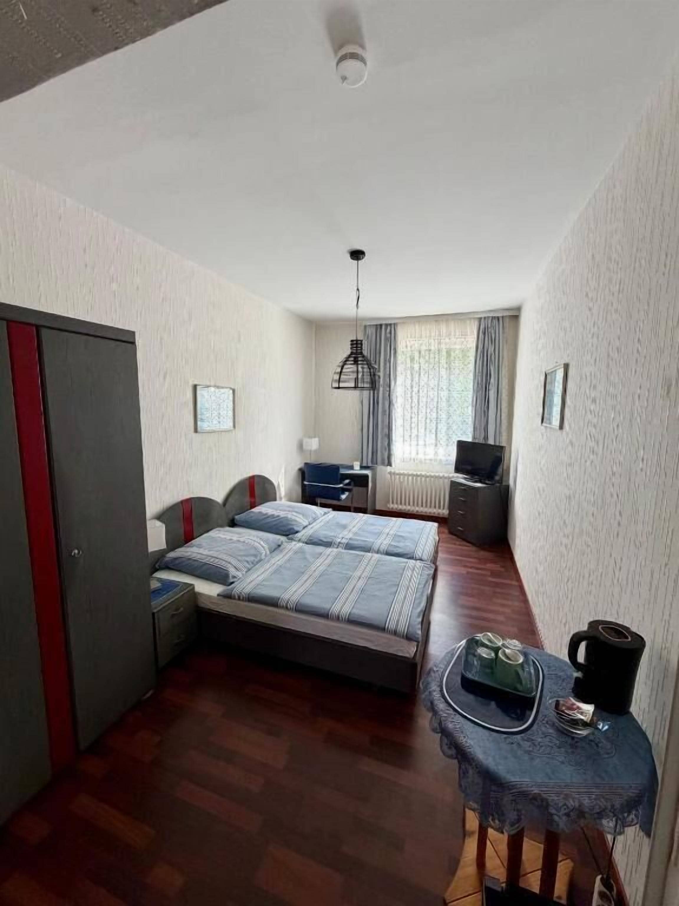 Un dormitorio con cama, mesita de noche, lámpara y ventana con cortinas.