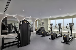A modern gym with cardio machines, weight machines, and a large mirror. - Marriott Dubai | Premium 1BR | Set Your Own Pace Near DIFC (Dubai)