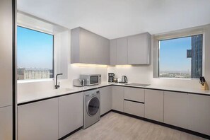 Una cucina moderna con lavatrice, forno a microonde e macchina del caffè, ampie finestre vista città e un design minimalista.
