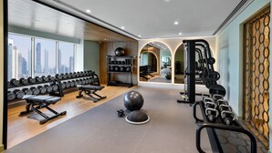 Ein Fitnessstudio mit Trainingsgeräten, einer Spiegelwand und Blick auf die Stadt.