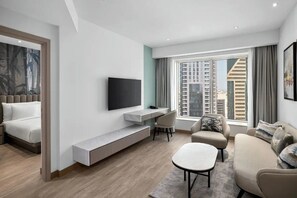 A modern living room with a TV, sofa, and dining area, featuring a city view through large windows.
