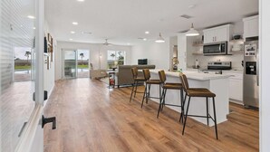 A modern kitchen with a bar area, wooden flooring, and a view of palm trees. - Al's Hideaway - Private Pool (Brunswick)