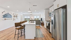 A modern kitchen with a central island, bar stools, a stainless steel refrigerator, and a large window. - Al's Hideaway - Private Pool (Brunswick)
