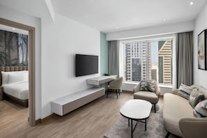 A modern living room with a TV, sofa, and dining area, featuring a city view through large windows.