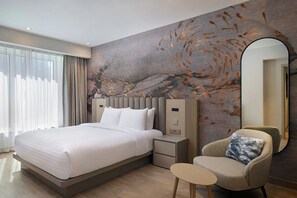 Habitación de hotel moderna con una cama grande, una silla, una mesita y una pared con diseño de hojas.