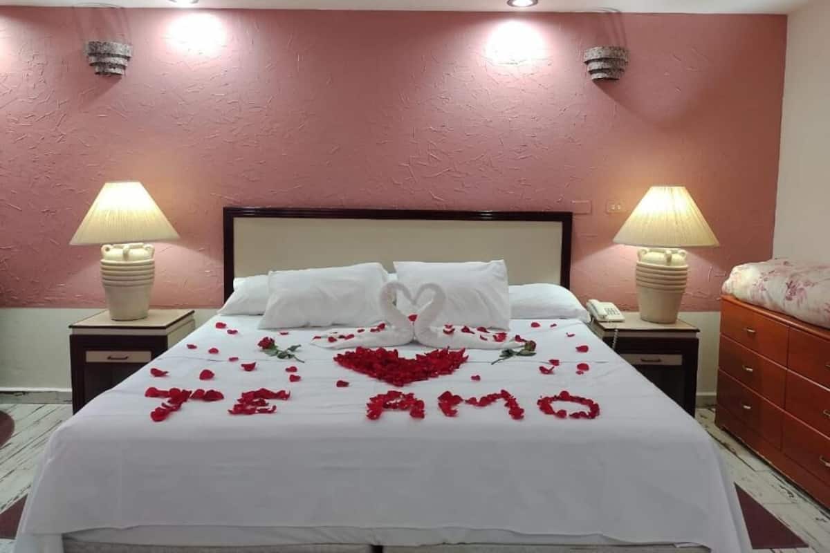 Habitación de hotel con una cama, dos lámparas de noche, un teléfono y una pared roja.