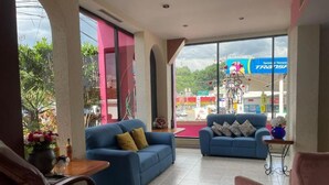 A hotel lobby with two blue sofas, a pink chair, a wooden table with a vase of flowers, and a view of a gas station outside. - HOTEL TAMAZUNCHALE (Tamazunchale)