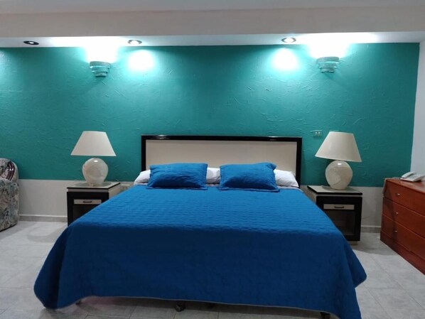 A bedroom with a bed, two bedside tables, a nightstand, a dresser, and a wall with a textured finish.