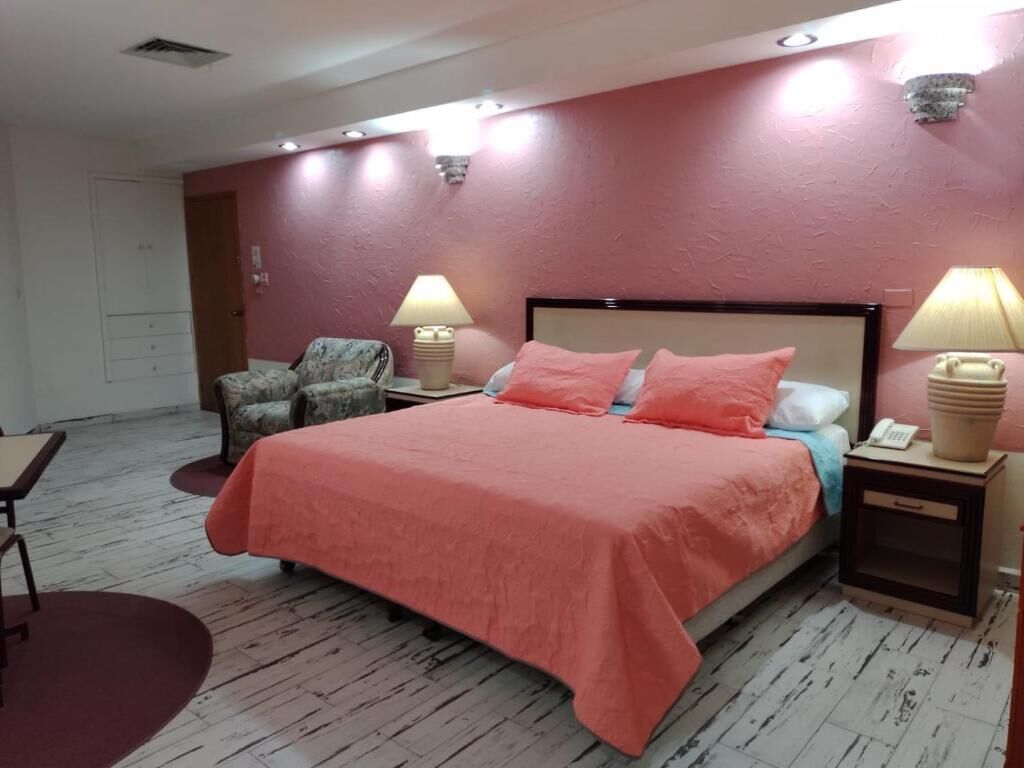 Un dormitorio con una cama, dos mesitas de noche con lámparas, una silla y una pequeña mesa.