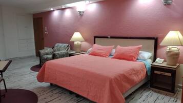 Un dormitorio con una cama, dos mesitas de noche con lámparas, una silla y una pequeña mesa.