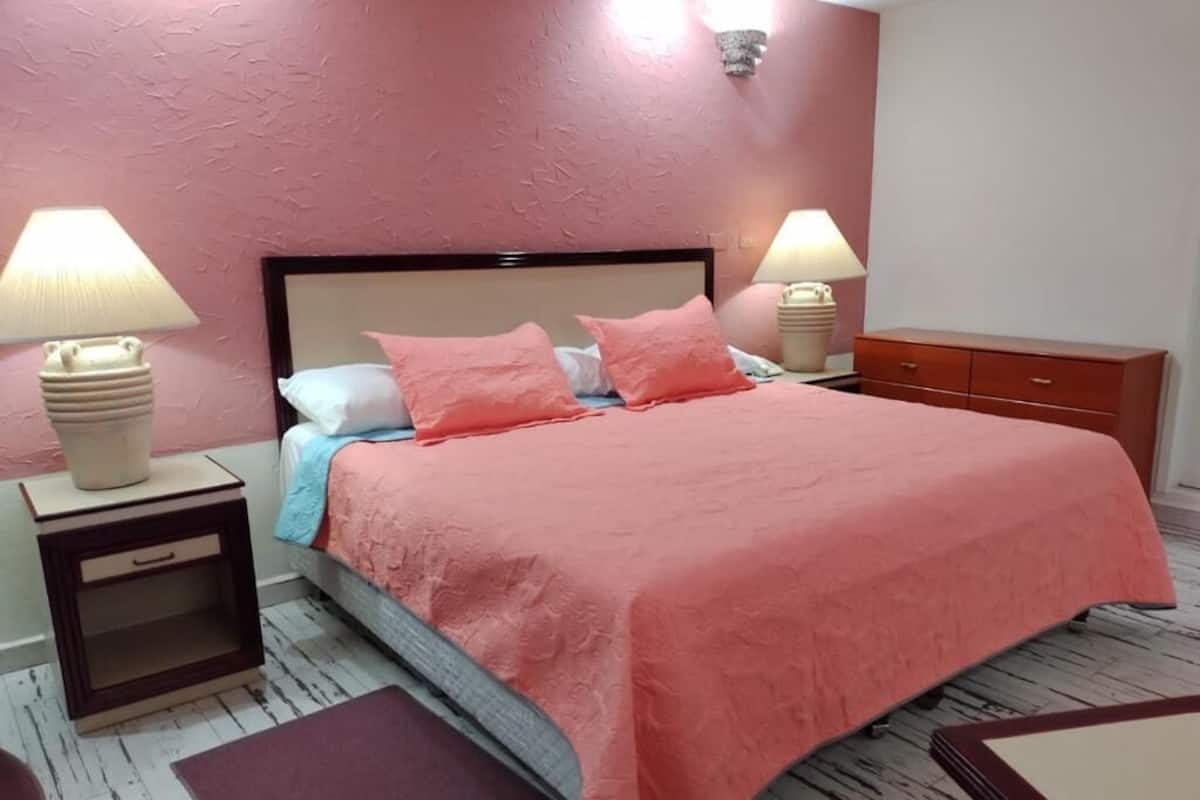 Un dormitorio con una cama, dos mesitas de noche con lámparas, un velador y suelo de madera.
