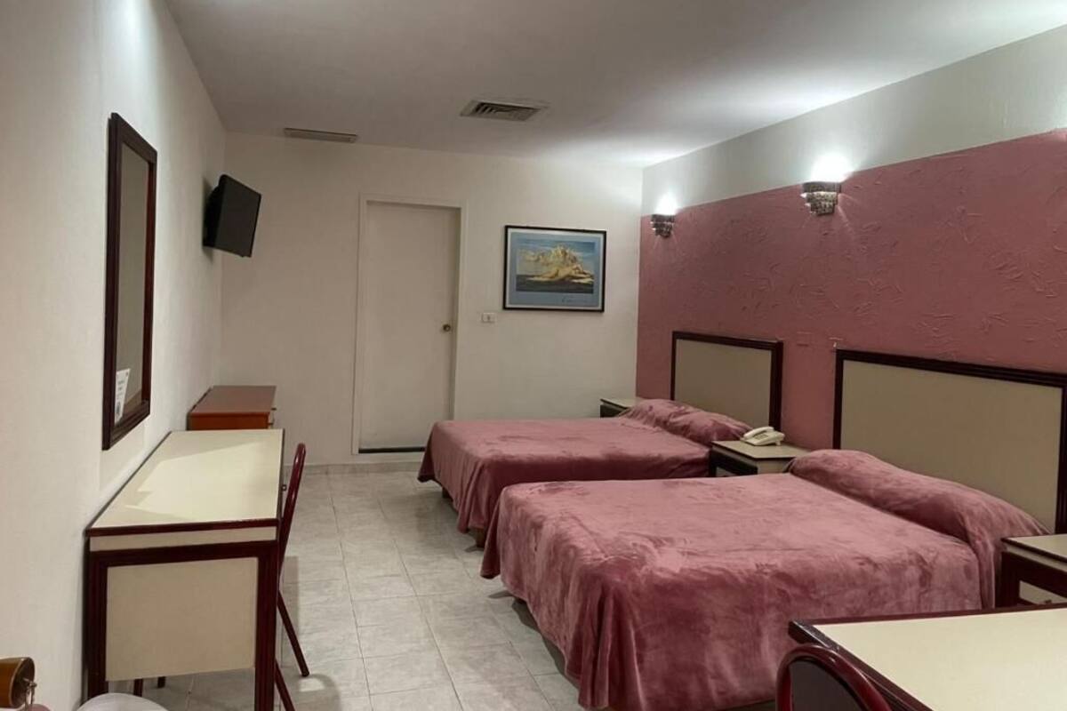 Habitación de hotel con dos camas, un escritorio, una silla, un televisor montado en la pared y una puerta.