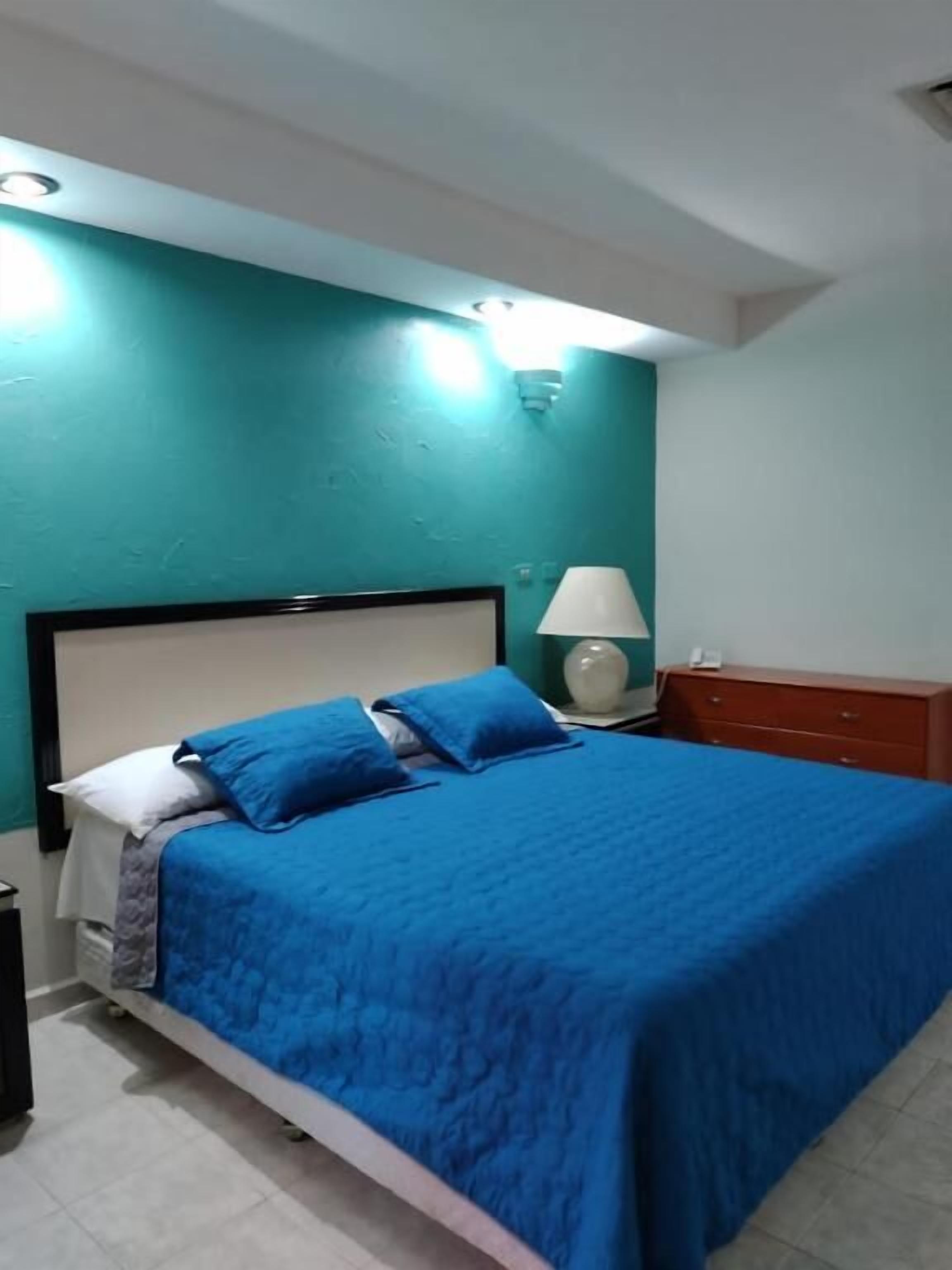 A bedroom with a bed, a nightstand, a lamp, and a dresser.