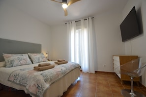 Ein Schlafzimmer mit einem Bett, einem Nachttisch, einer Lampe, einem Fernseher und einem Sessel.