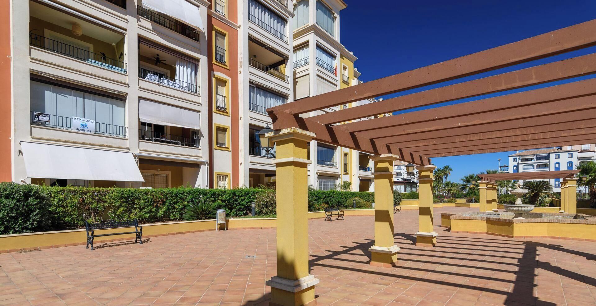 Ein mehrstöckiges Wohngebäude mit Balkonen, einem gepflasterten Innenhof und einer Pergola.