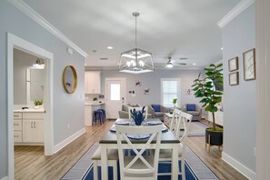 A modern dining area with a geometric chandelier, a round mirror, and a dining table set for four. - Spacious Gulf Shores Beach House With Private Patio and Pool Access (Gulf Shores)