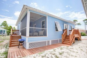 Ein blaues Haus mit Veranda, Holztreppe und Grill.