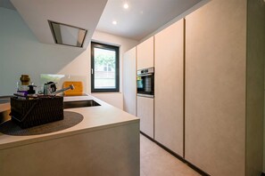 Una cocina moderna con horno integrado, una ventana y una encimera con un lavabo y una tabla de cortar de madera.