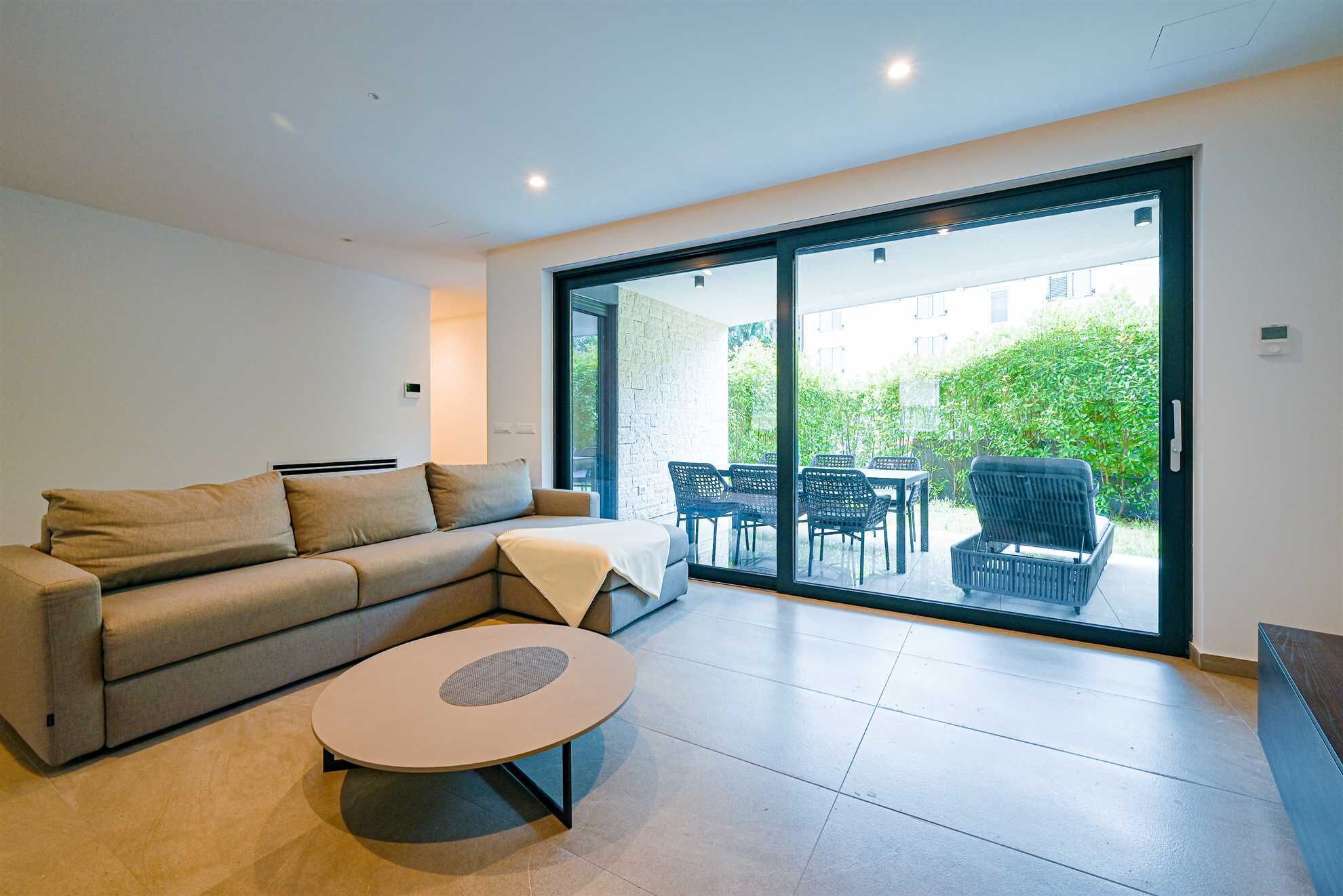 A modern living room with a sofa, a round coffee table, and a sliding glass door leading to an outdoor patio area.