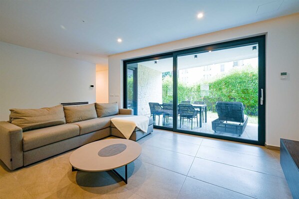 Una sala de estar moderna con un sofá, una mesa redonda de centro y una puerta corrediza de vidrio que da a un patio exterior.