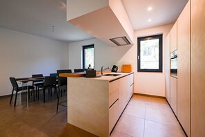 Eine moderne Küche mit einer zentralen Kochinsel, einem Essbereich mit Stühlen und einem Fenster, das für natürliches Licht sorgt.