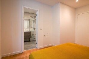Un dormitorio con una cama, una puerta que da a un baño y una pared blanca.